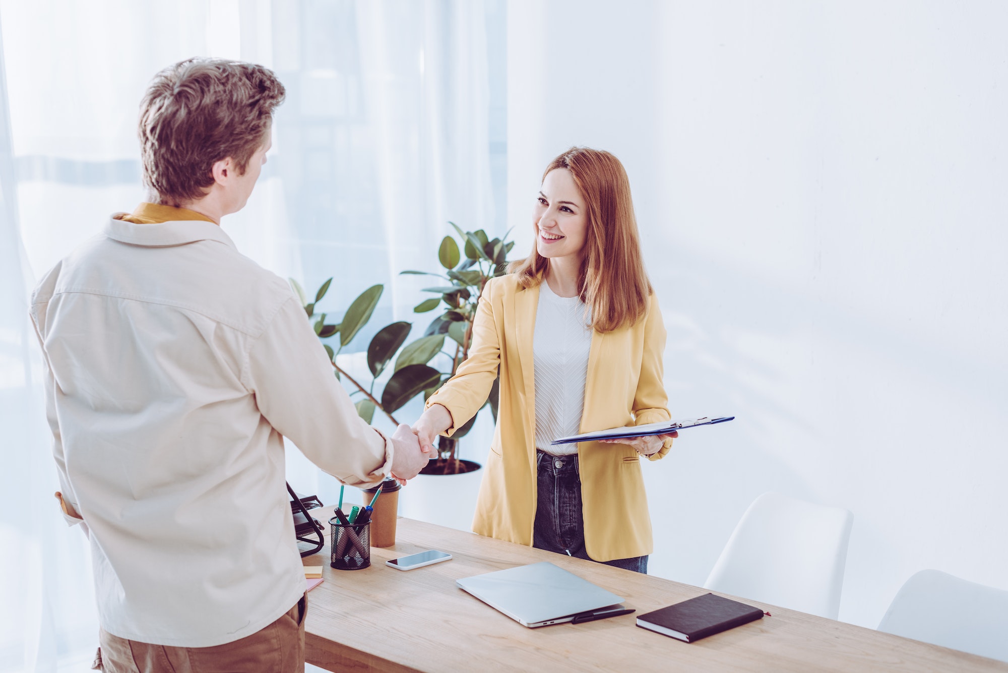 happy-recruiter-holding-clipboard-and-shaking-hands-with-employee-in-modern-office.jpg